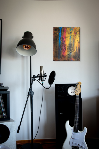 Ein Wohnzimmer mit Mikrophon, Gitarre, Lampe und modernem Kunstwerk an der Wand.