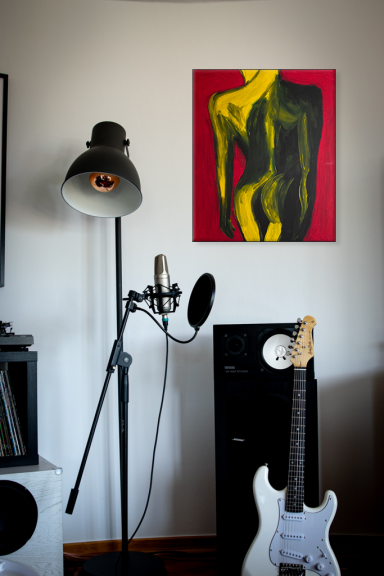 Eine Stehlampe und ein Mikrofon neben einer Gitarre vor einer Wand mit einem gemalten Akt.