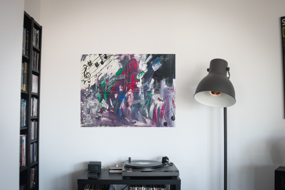 Buntes abstraktes Gemälde an einer weißen Wand über einem Plattenspieler und einer Lampe.